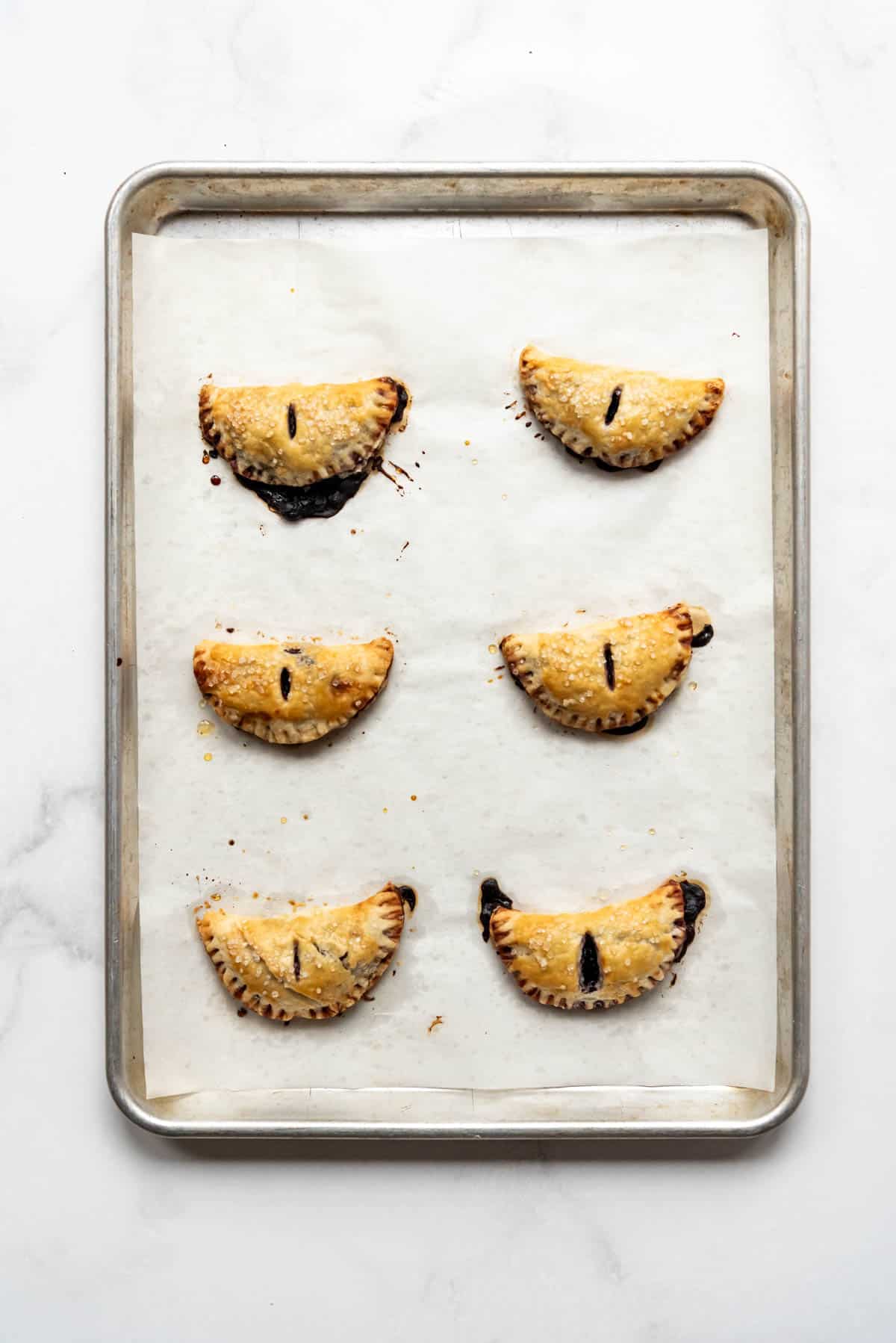 Baked blueberry hand pies on a baking sheet.