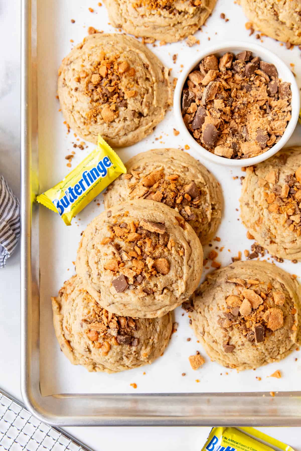 An overhead image of butterfingers cookies on a baking sheet with fun size butterfingers candy bars near them.