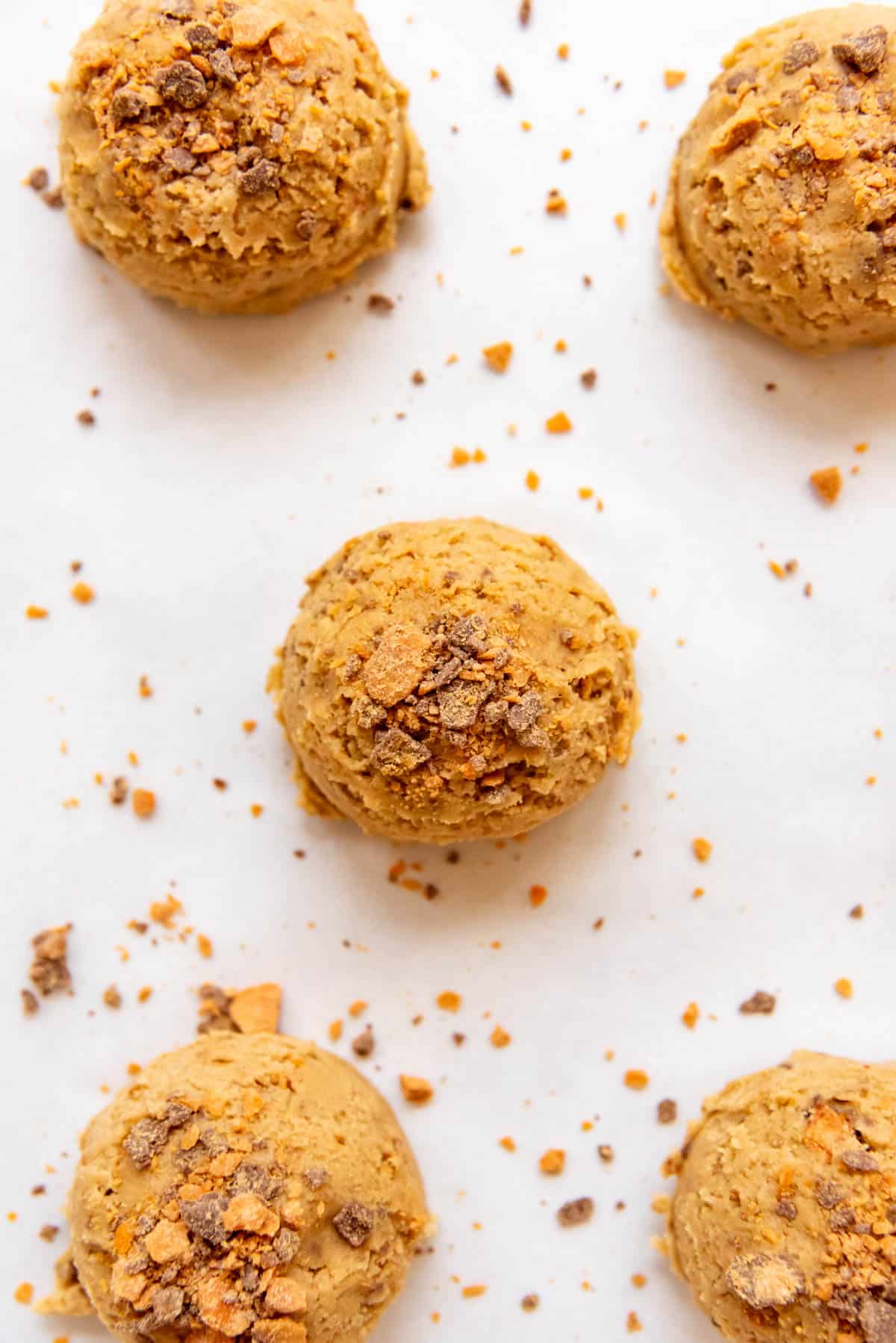 Balls of butterfingers cookie dough with more crushed butterfingers pressed on top.
