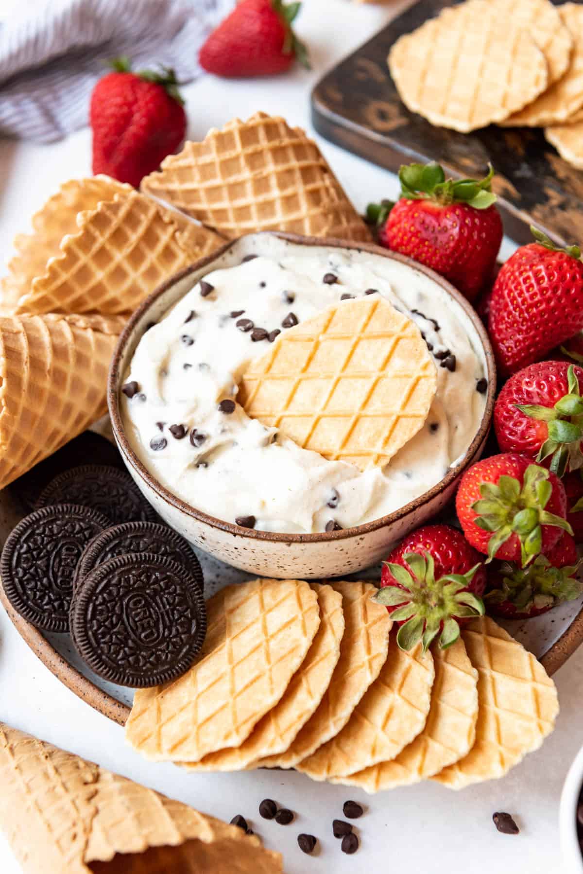 A bowl of cannoli dessert dip with fruit and cookie dippers surrounding it.