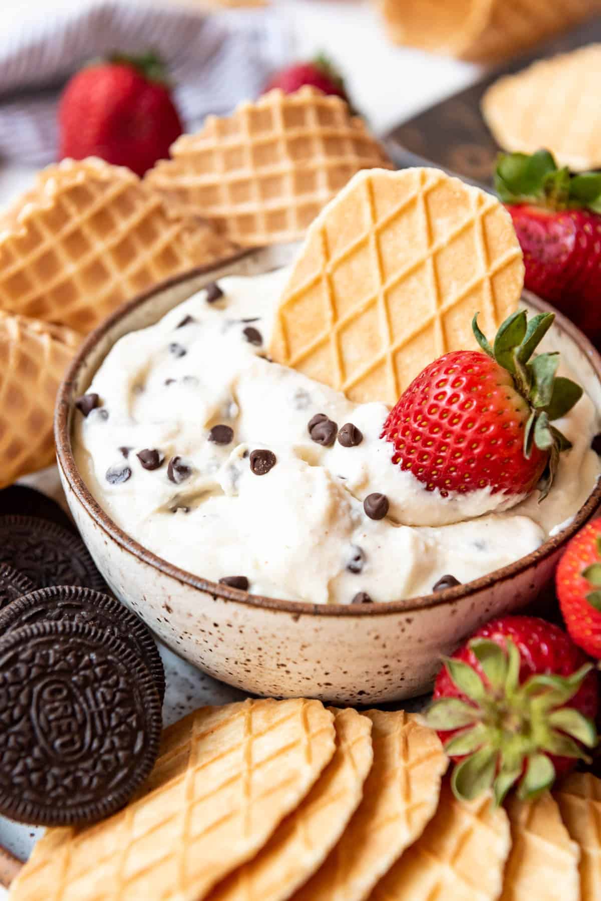 A close image of a bowl of cannoli dip with a wafer cookie and strawberry in it.