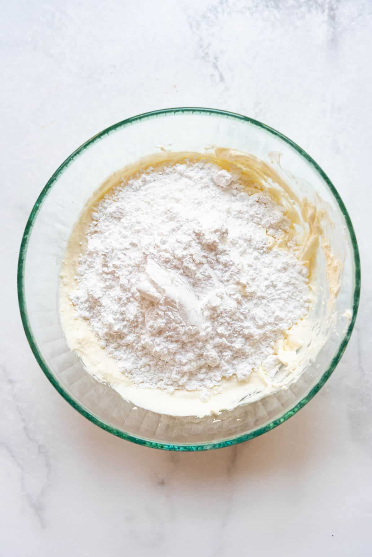 Adding powdered sugar to mascarpone cheese in a large mixing bowl.