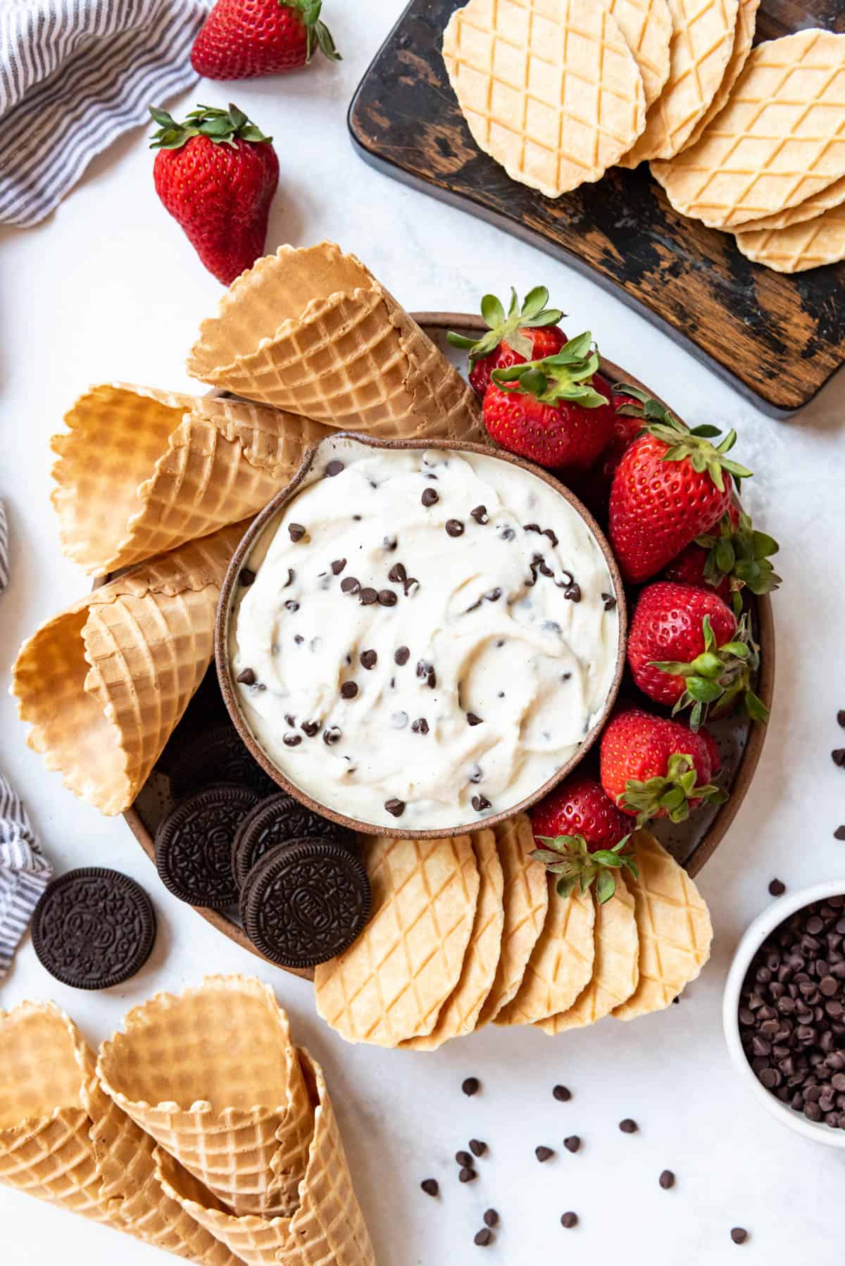 A bowl of cannoli dip with waffle biscuit cookies, strawberries, and Oreos around it.