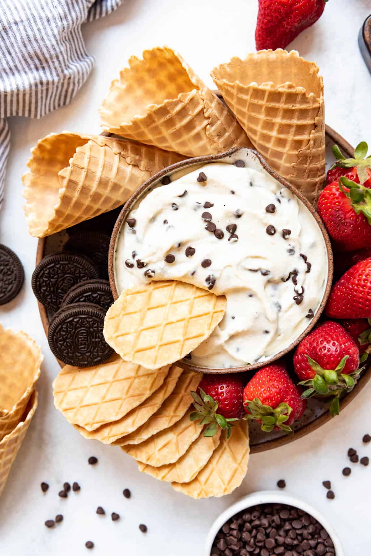 An overhead image of cannoli dessert dip surrounded by strawberries, Oreos, and waffle cones.