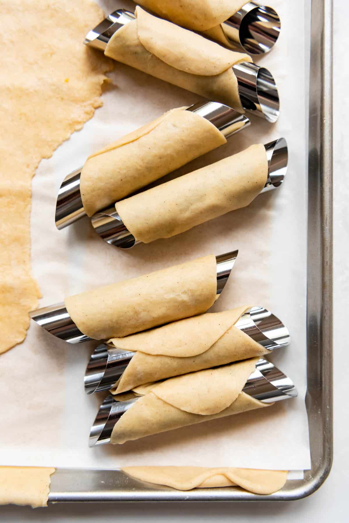 Cannoli dough wrapped around metal cannoli forms before frying.