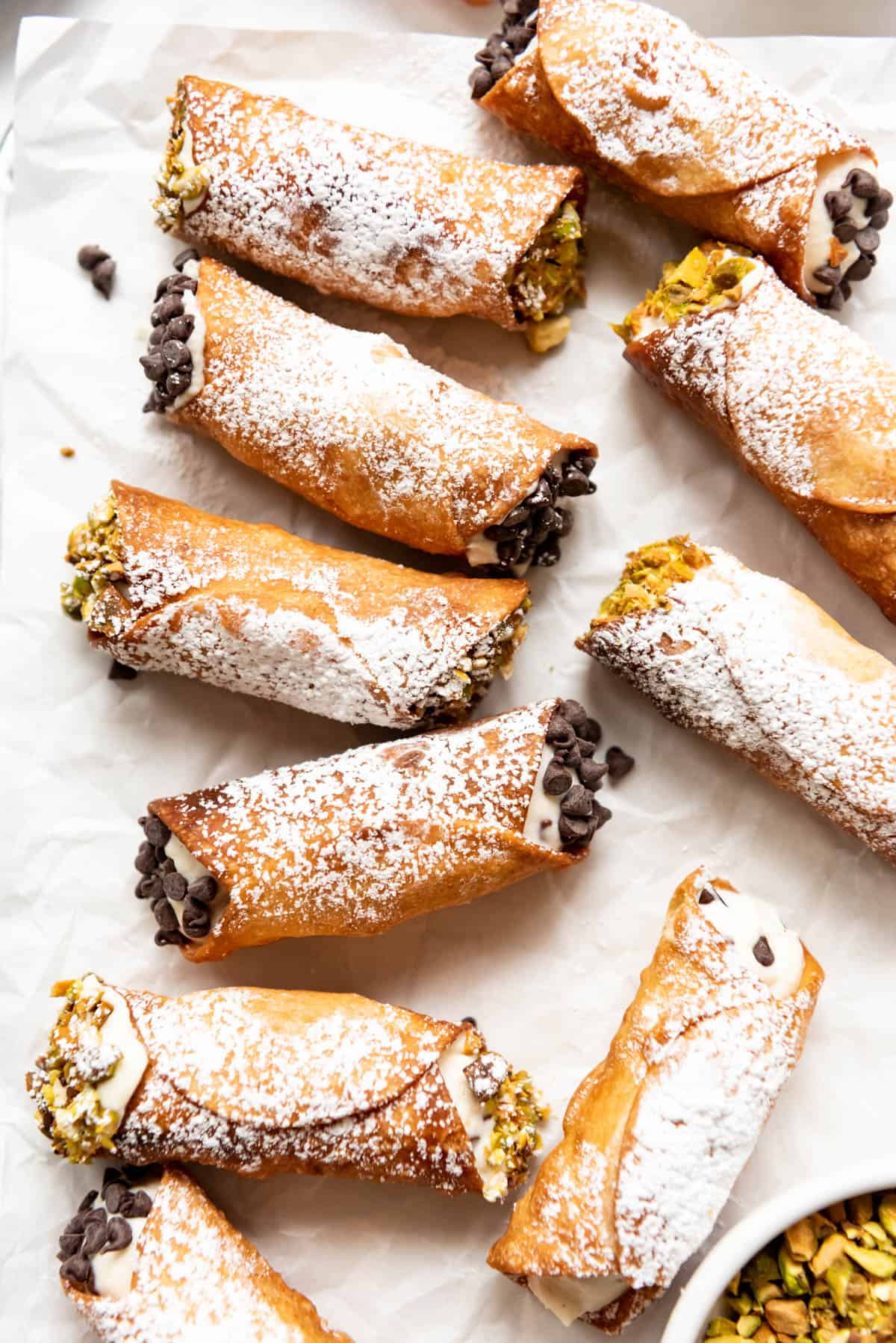 Cannoli dusted with powdered sugar and finished with chopped pistachios and mini chocoalte chips on the ends.