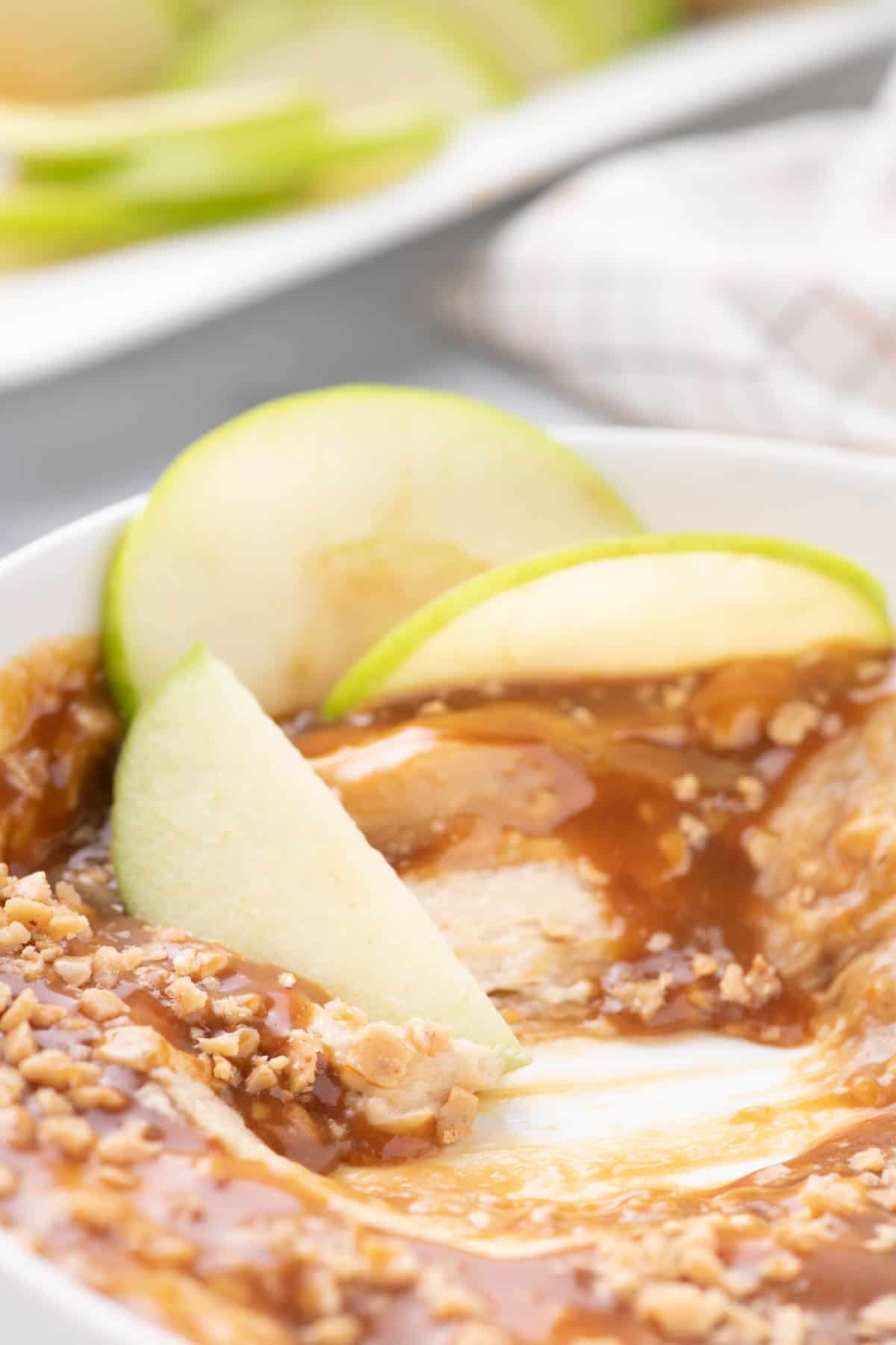 Close up of caramel apple dip in a white serving dish with apple slices in the top.