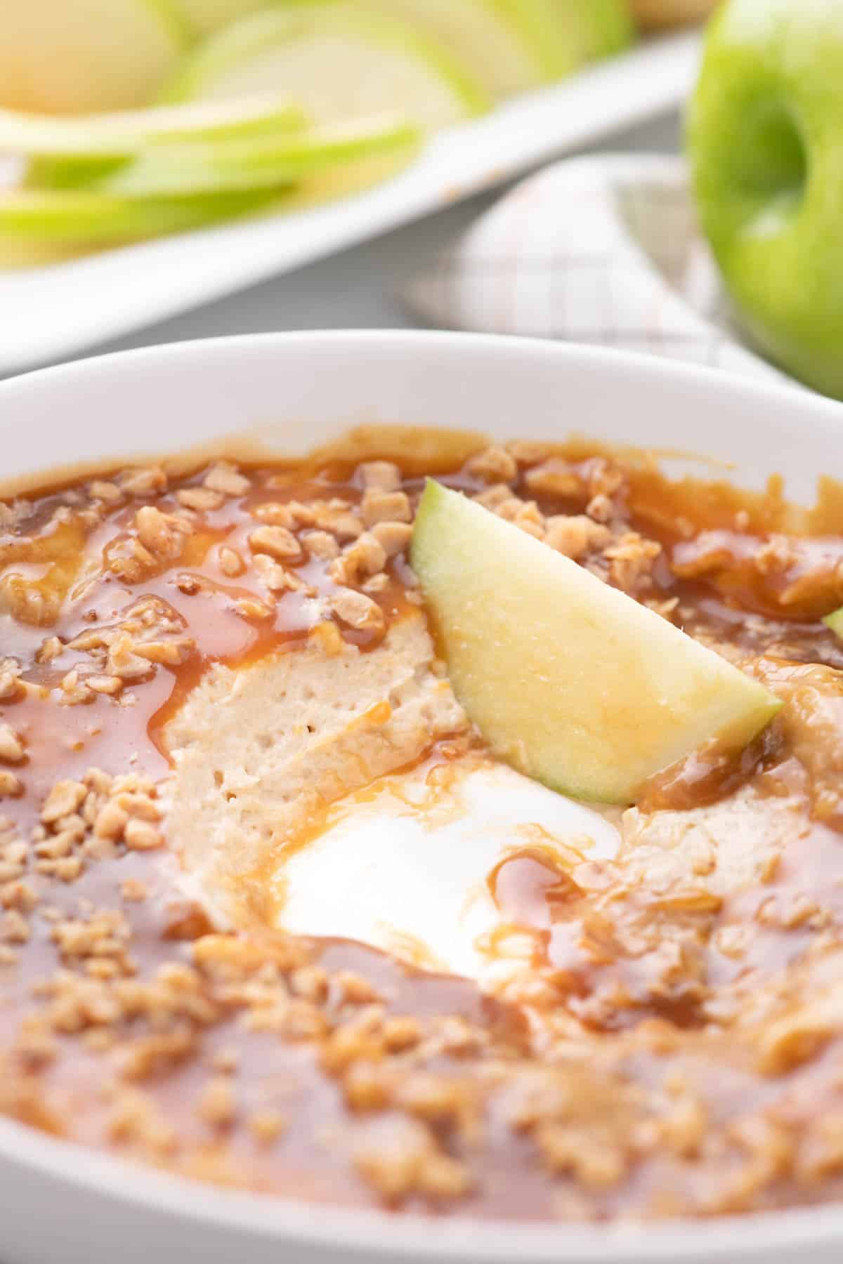 Close up of caramel apple dip in a white serving dish with apple slices in the top.