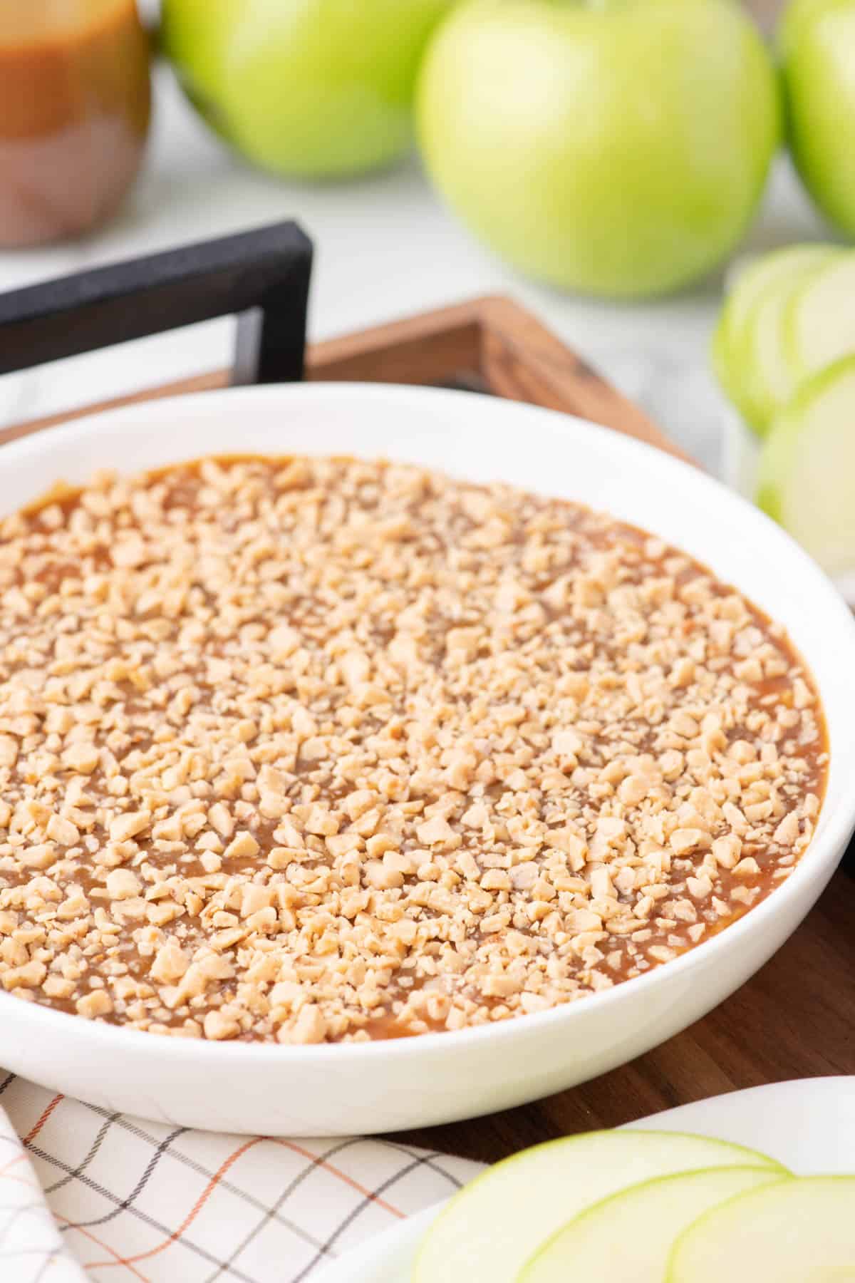 Caramel apple dip with a top crispy layer next to apples.