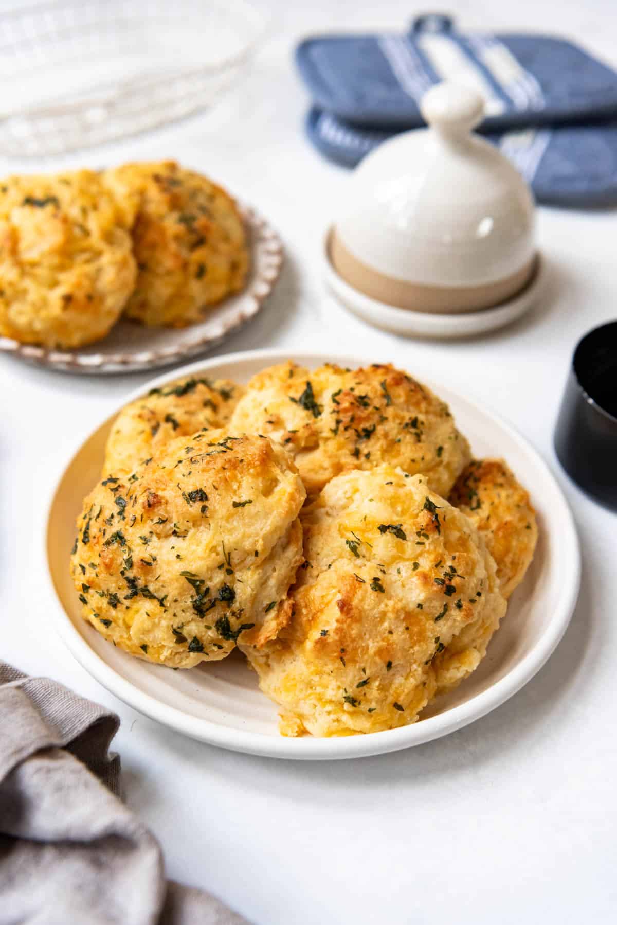 An image of plates of cheddar bay biscuits in front of a butter dish and blue hot pads.