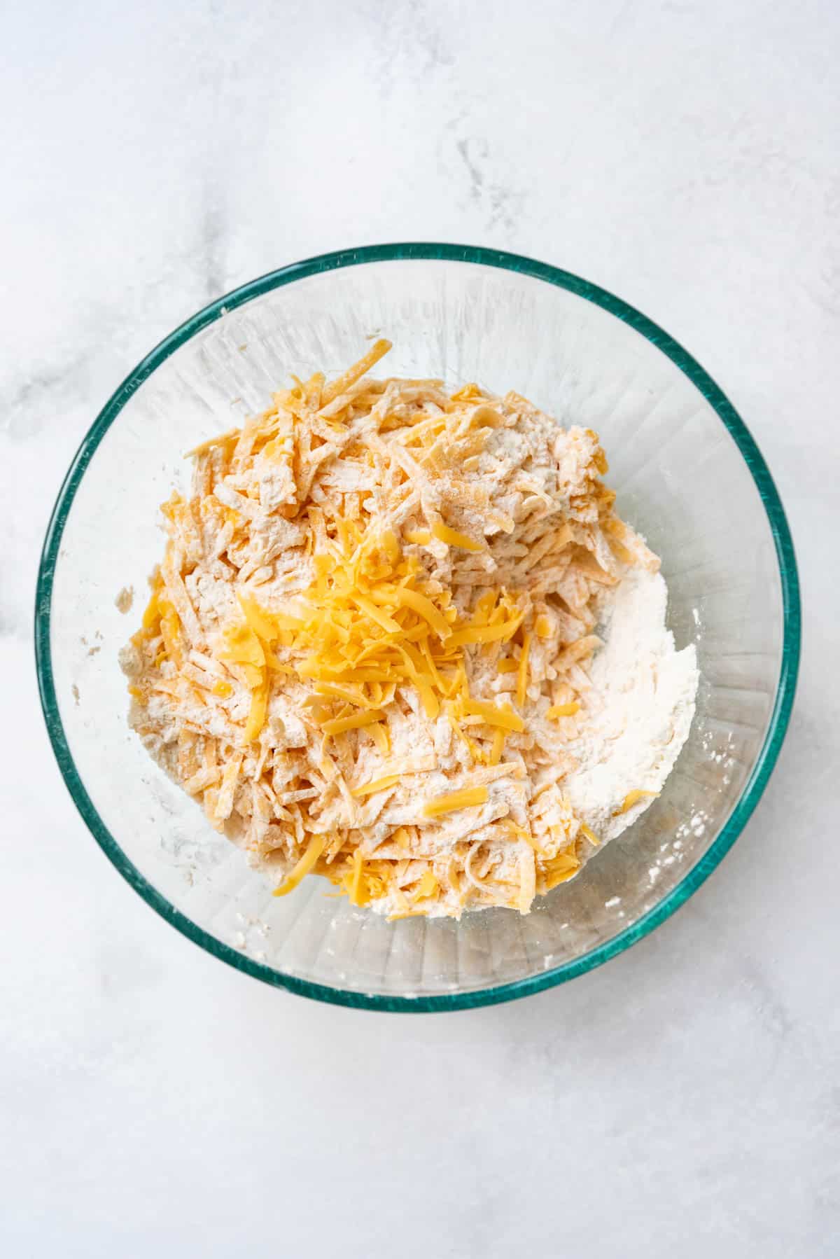 Combining grated cheese with flour, baking powder, baking soda, and salt in a large mixing bowl.