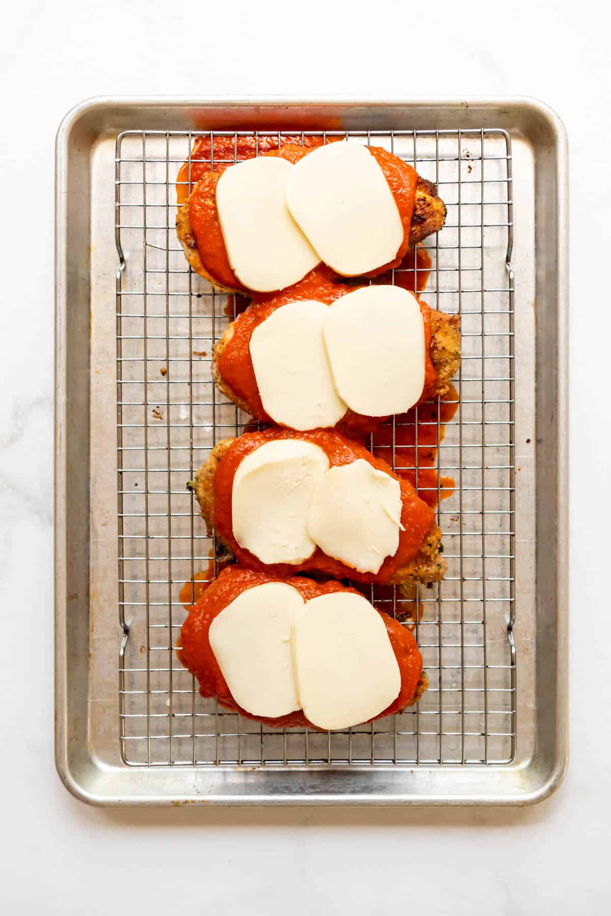 Adding slices of fresh mozzarella on top of chicken breasts and tomato sauce to make chicken parmesan.