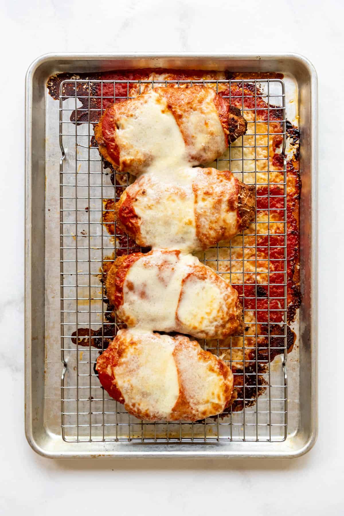 Baked chicken parmesan on a wire rack set over a baking sheet.