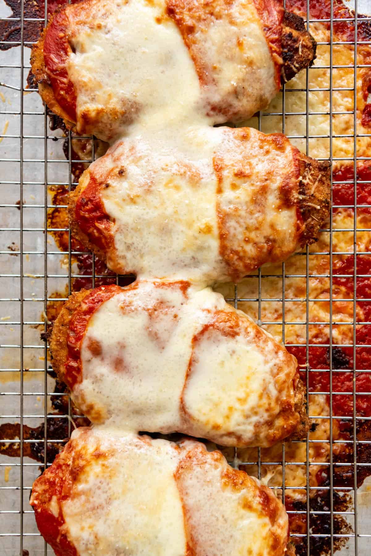 An overhead image of chicken parmesan with melted cheese on top on a wire rack.
