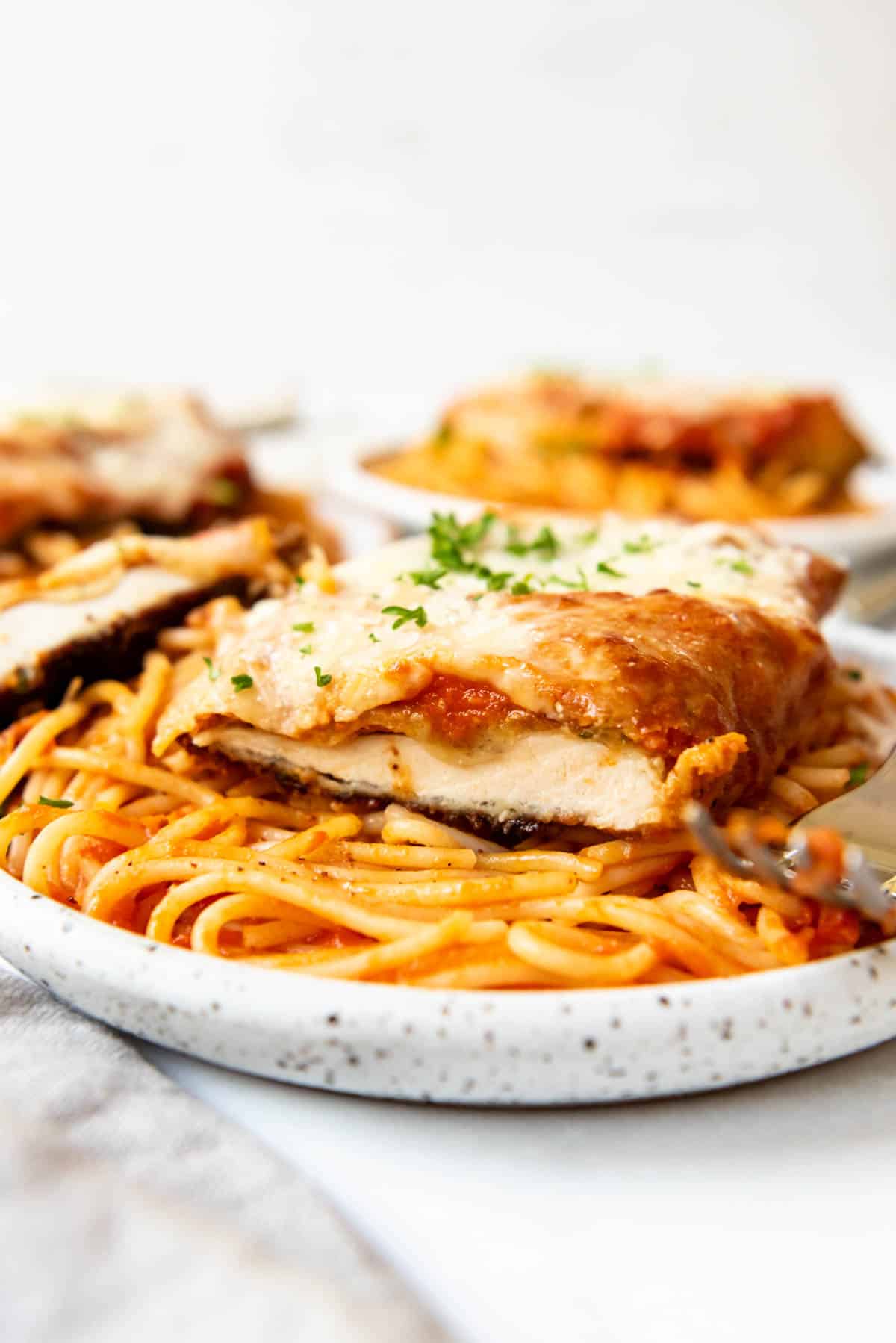Sliced chicken parmesan on a bed of spaghetti tossed in tomato saucer.