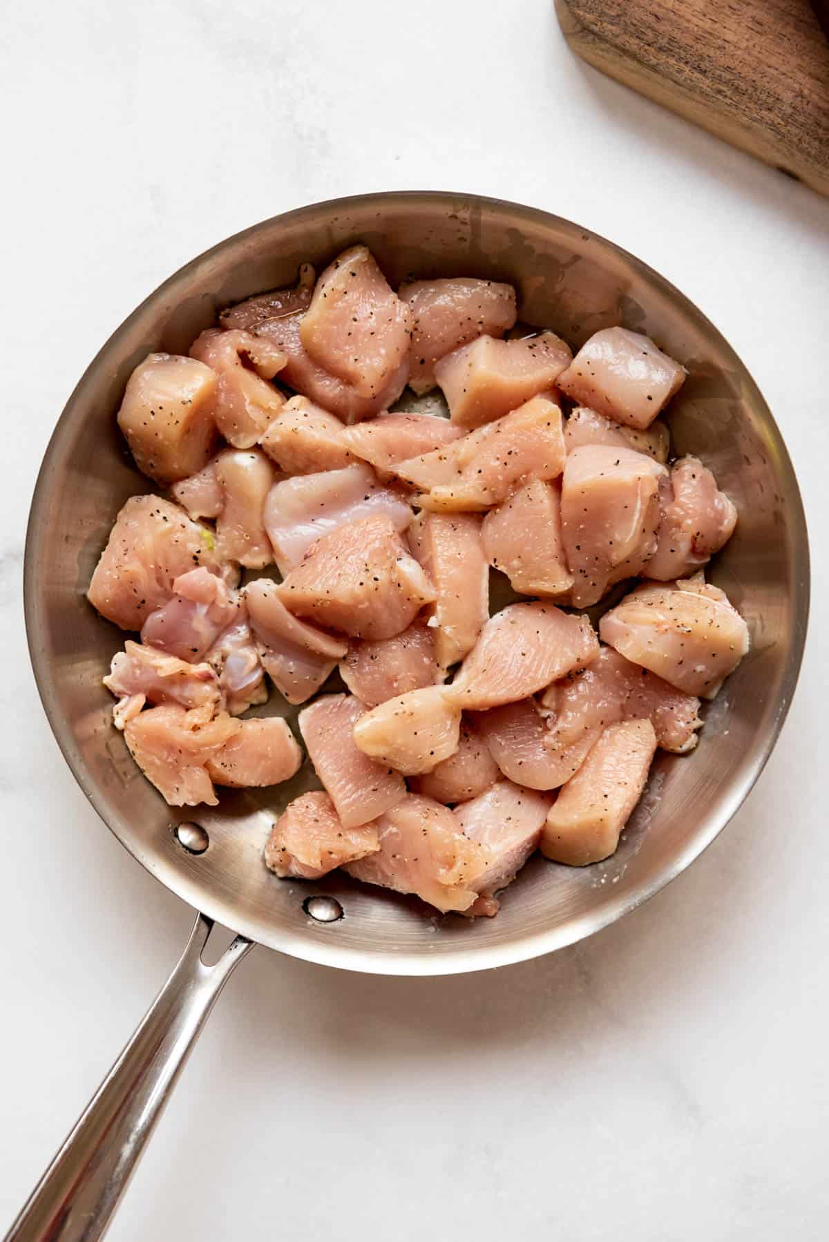 Seasoned chunks of chicken searing in a large pan.