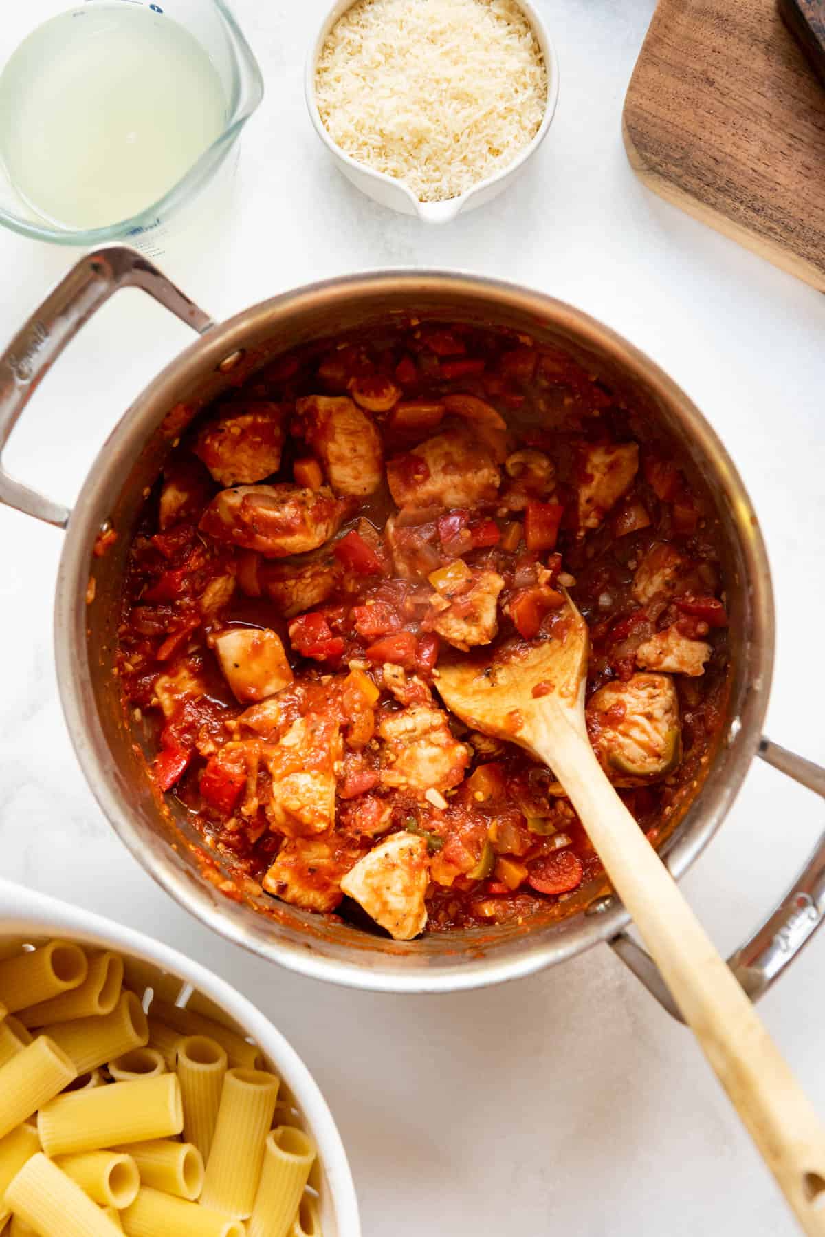Combining a tomato and veggie sauce with seared chicken breast pieces in a large pot.