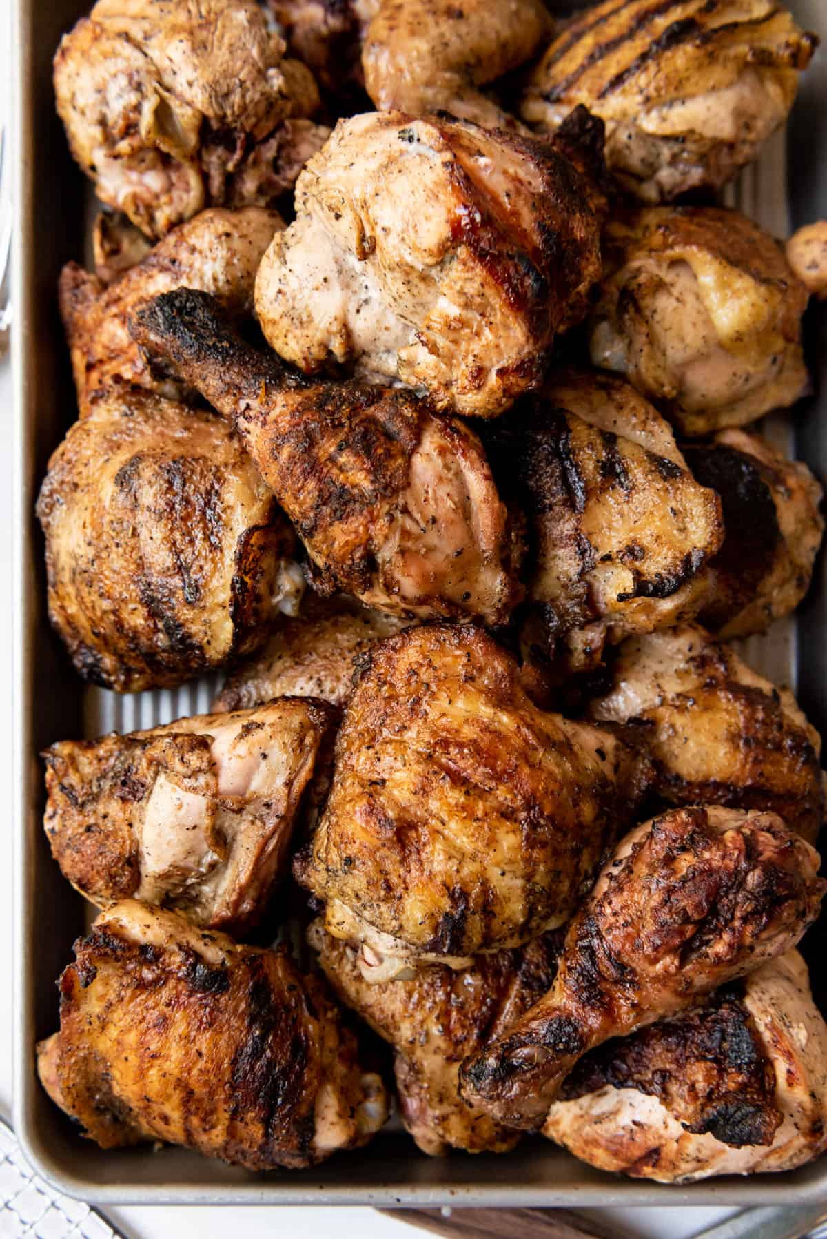 Pieces of grilled fireman's chicken piled on a baking sheet.
