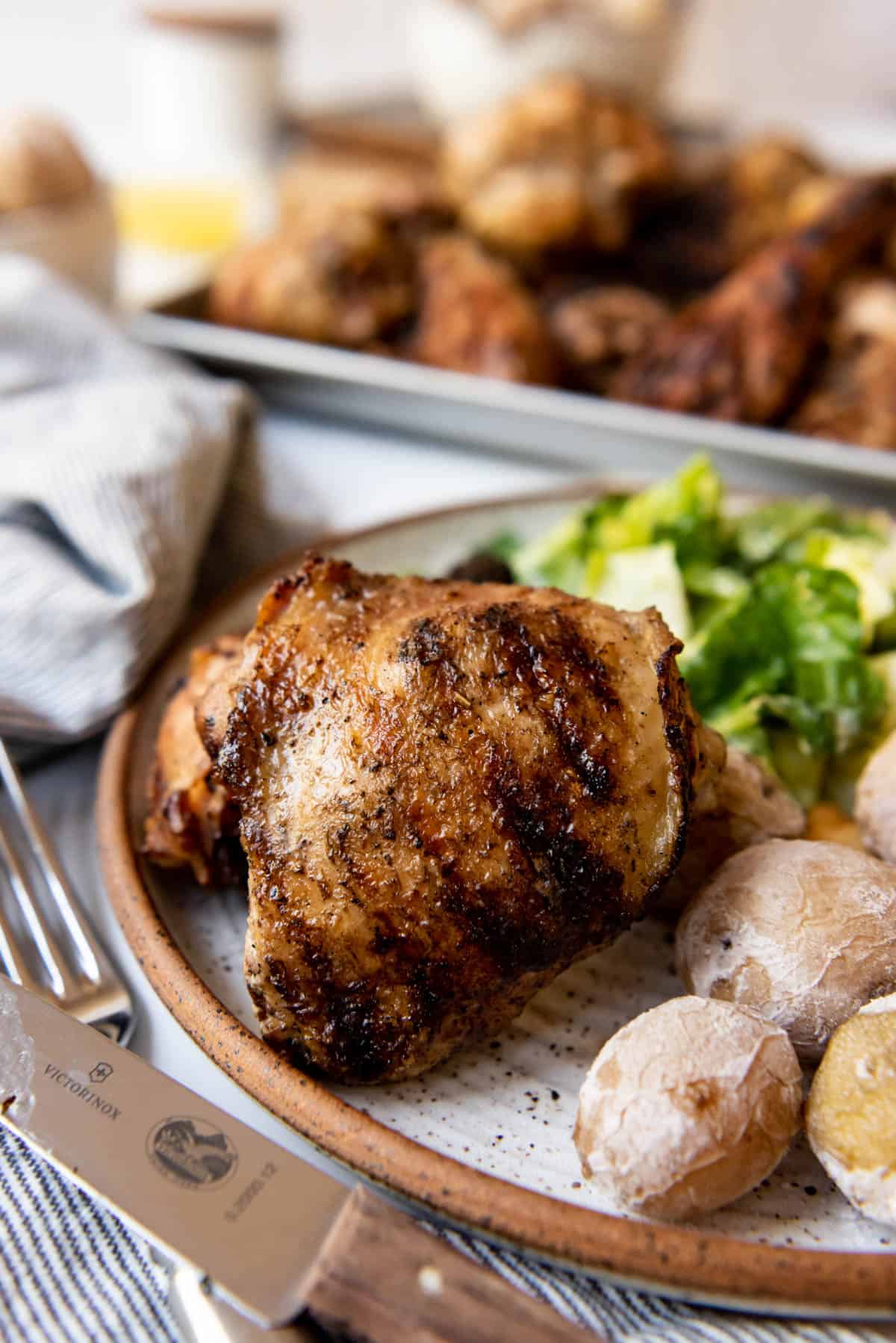A grilled Cornell chicken thigh on a plate with Syracuse salt potatoes.