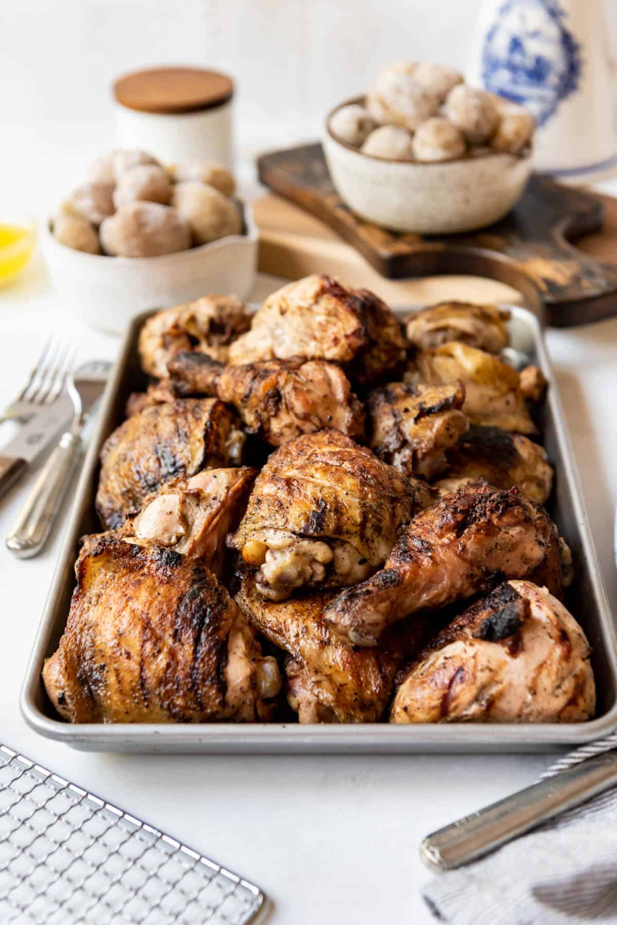 Grilled marinated Cornell chicken on a baking sheet in front of bowls of Syracuse salt potatoes.