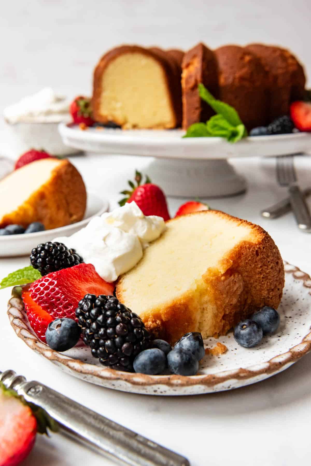 A slice of cream cheese pound cake on a plate with fresh fruit and whipped cream.
