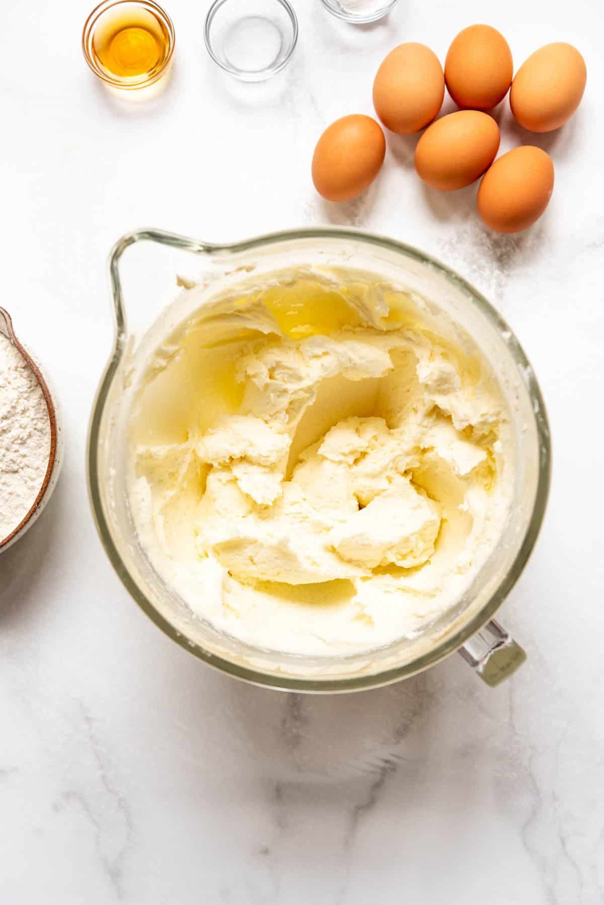 Creamed butter, cream cheese, and sugar in a bowl next to eggs, vanilla, and salt.