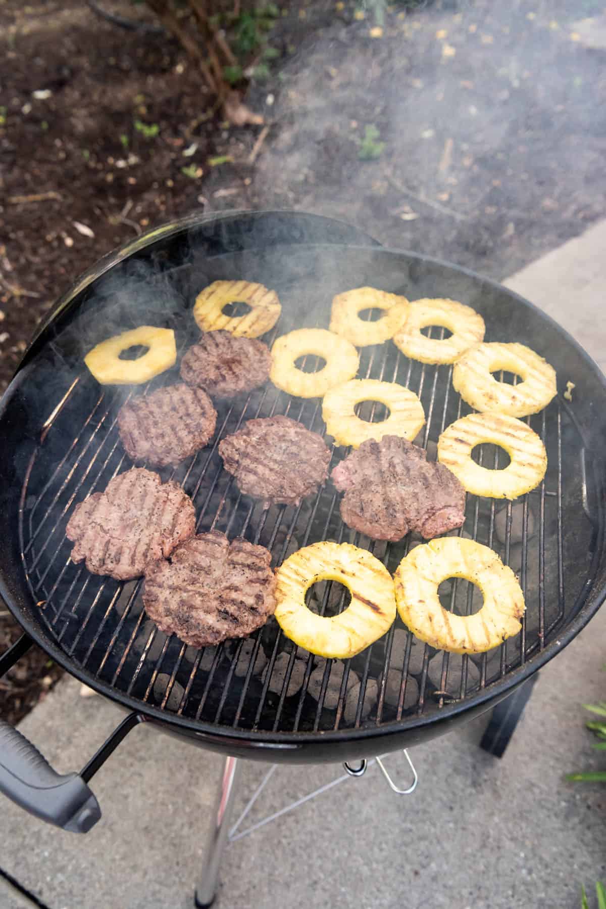 Grilling burgers and pineapple rings on a charcoal grill.