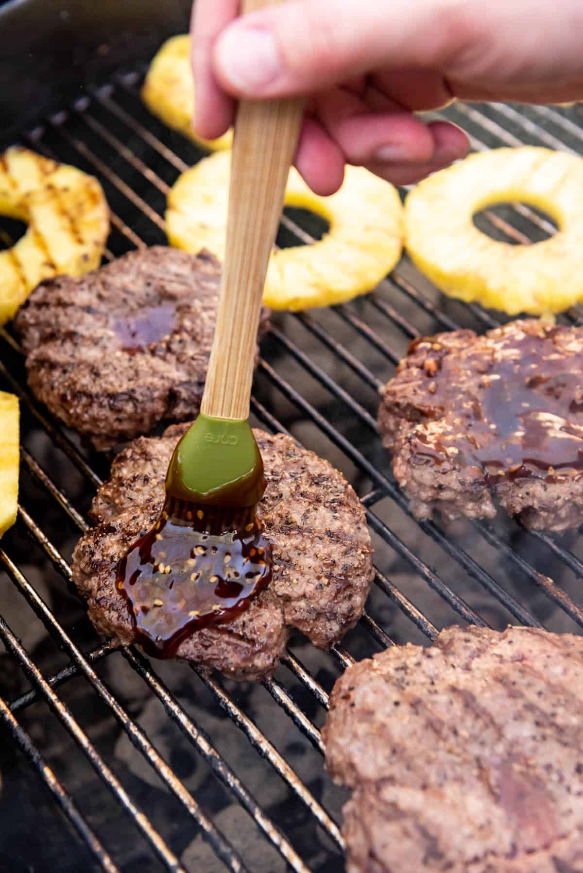Brushing burgers with teriyaki sauce while they are finishing on the grill before adding cheese.