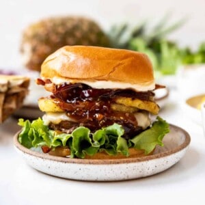 An image of a Hawaiian burger with grilled pineapple and teriyaki sauce in front of a whole pineapple.