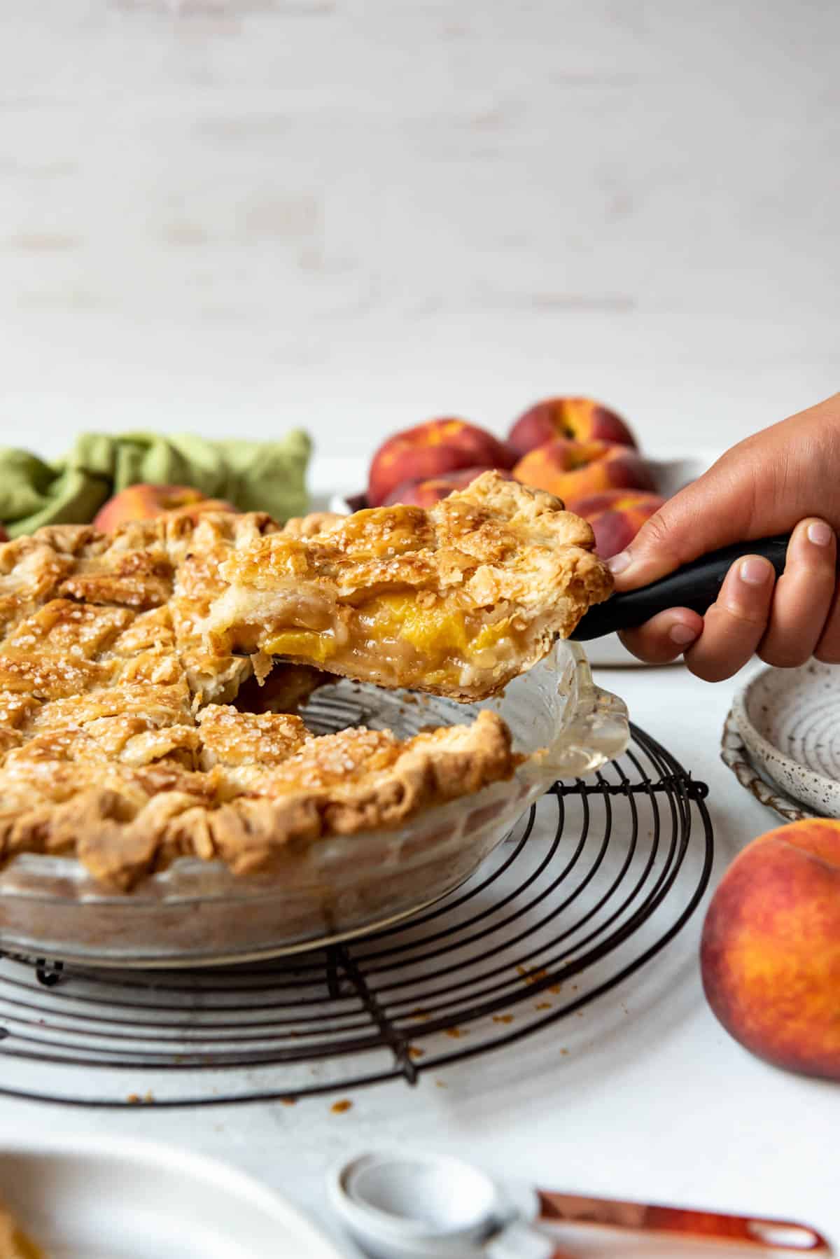 A hand lifting a slice of peach pie from the baking dish.