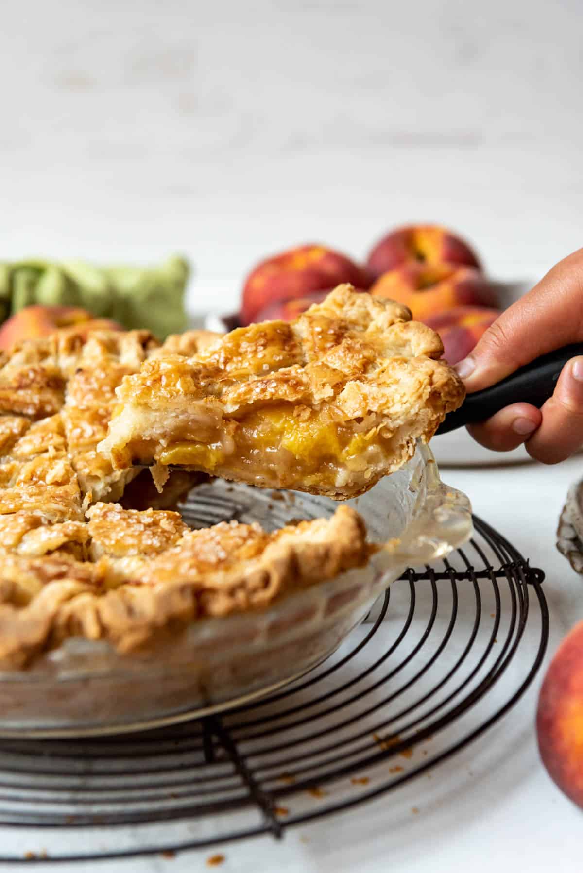 A hand lifting a slice of homemade peach pie from the pie dish.