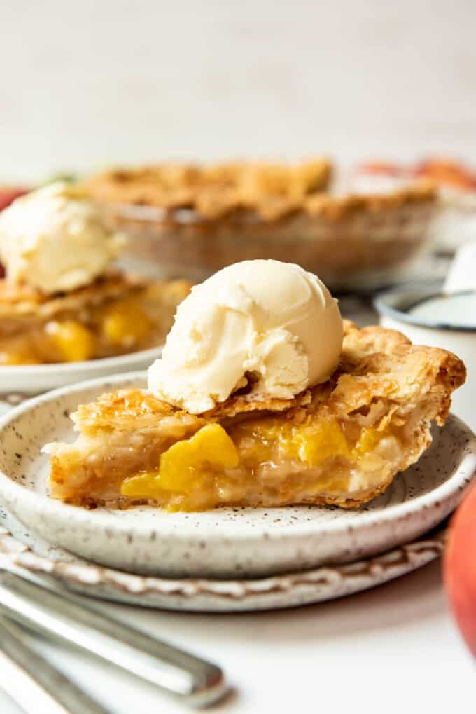 A close image of a slice of peach pie with a scoop of vanilla ice cream on top.