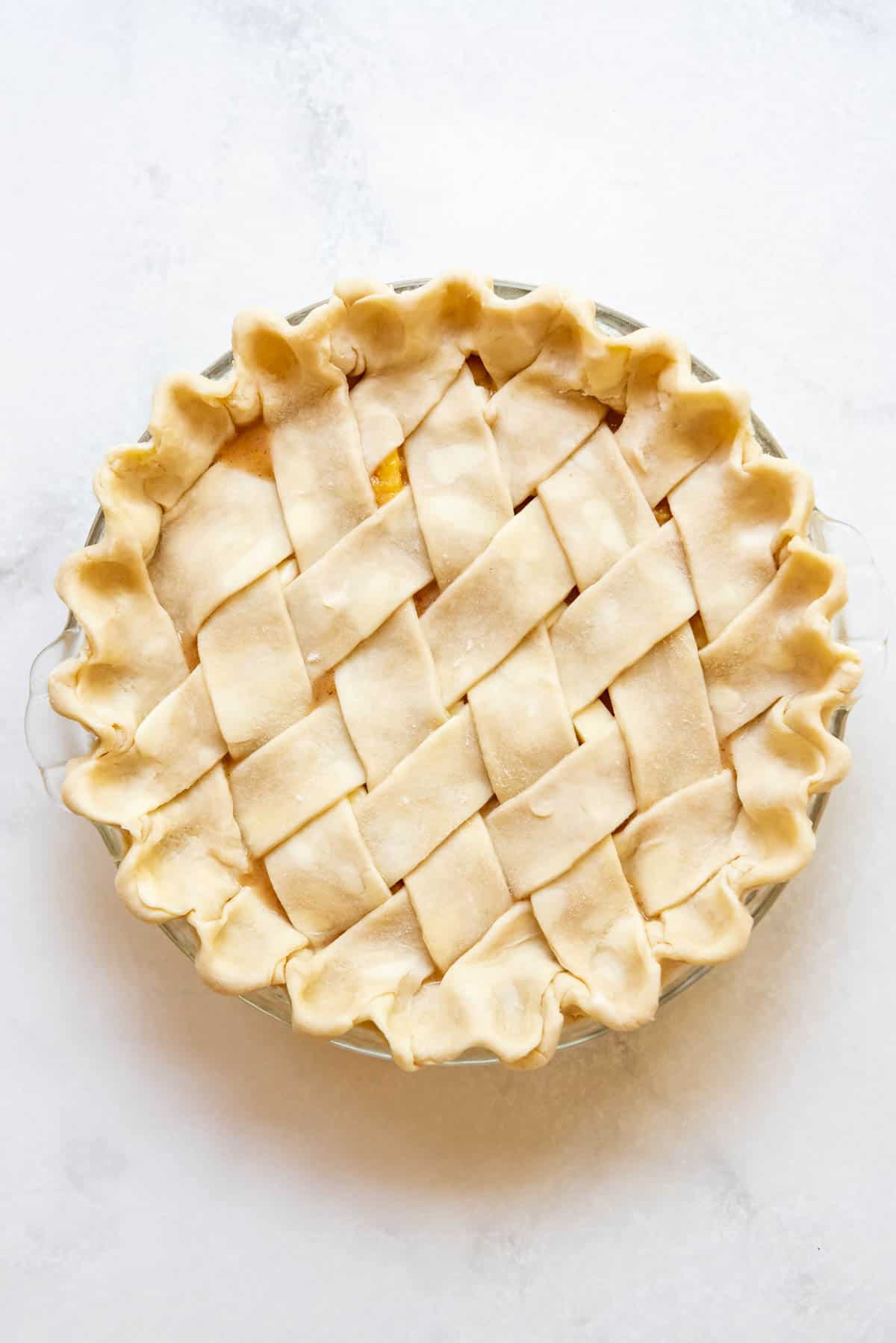 An unbaked peach pie with a lattice pie crust.