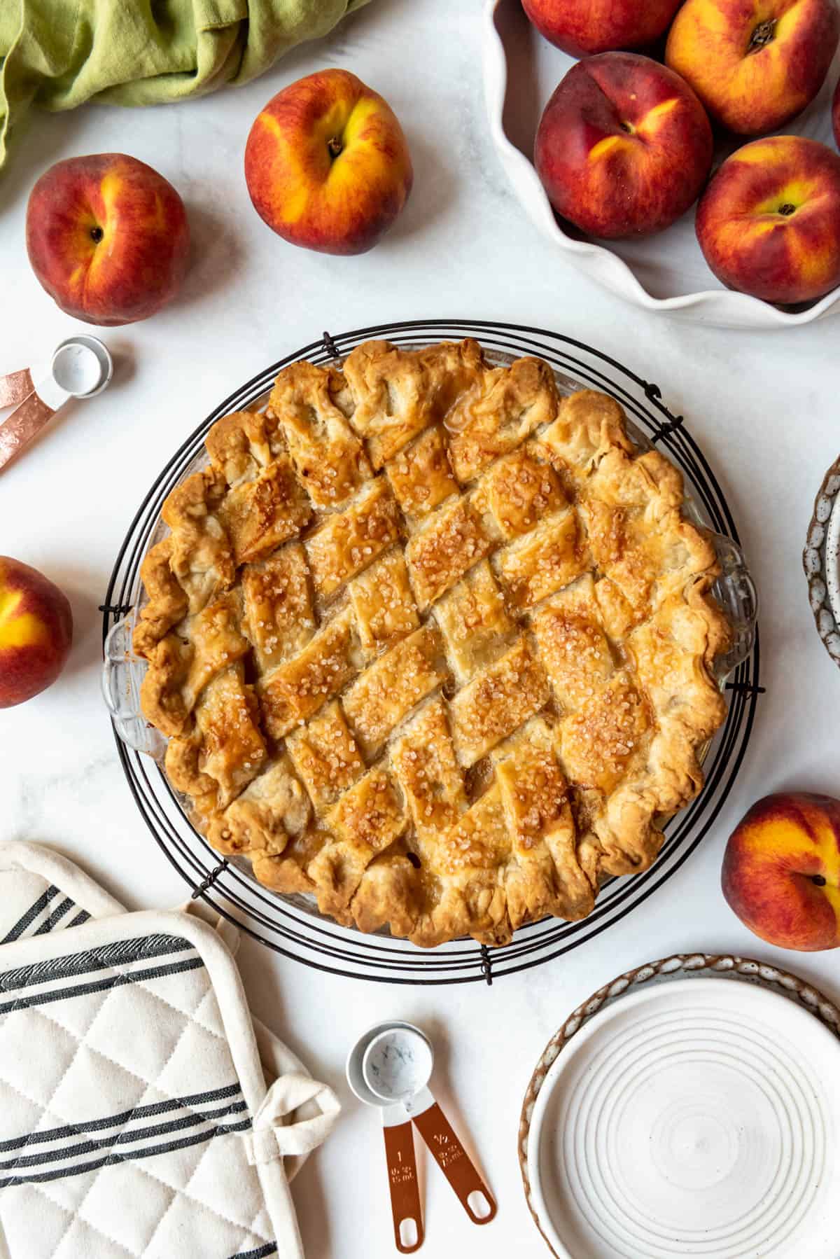 An overhead image of a baked peach pie with a lattice pie crust surrounded by fresh peaches.