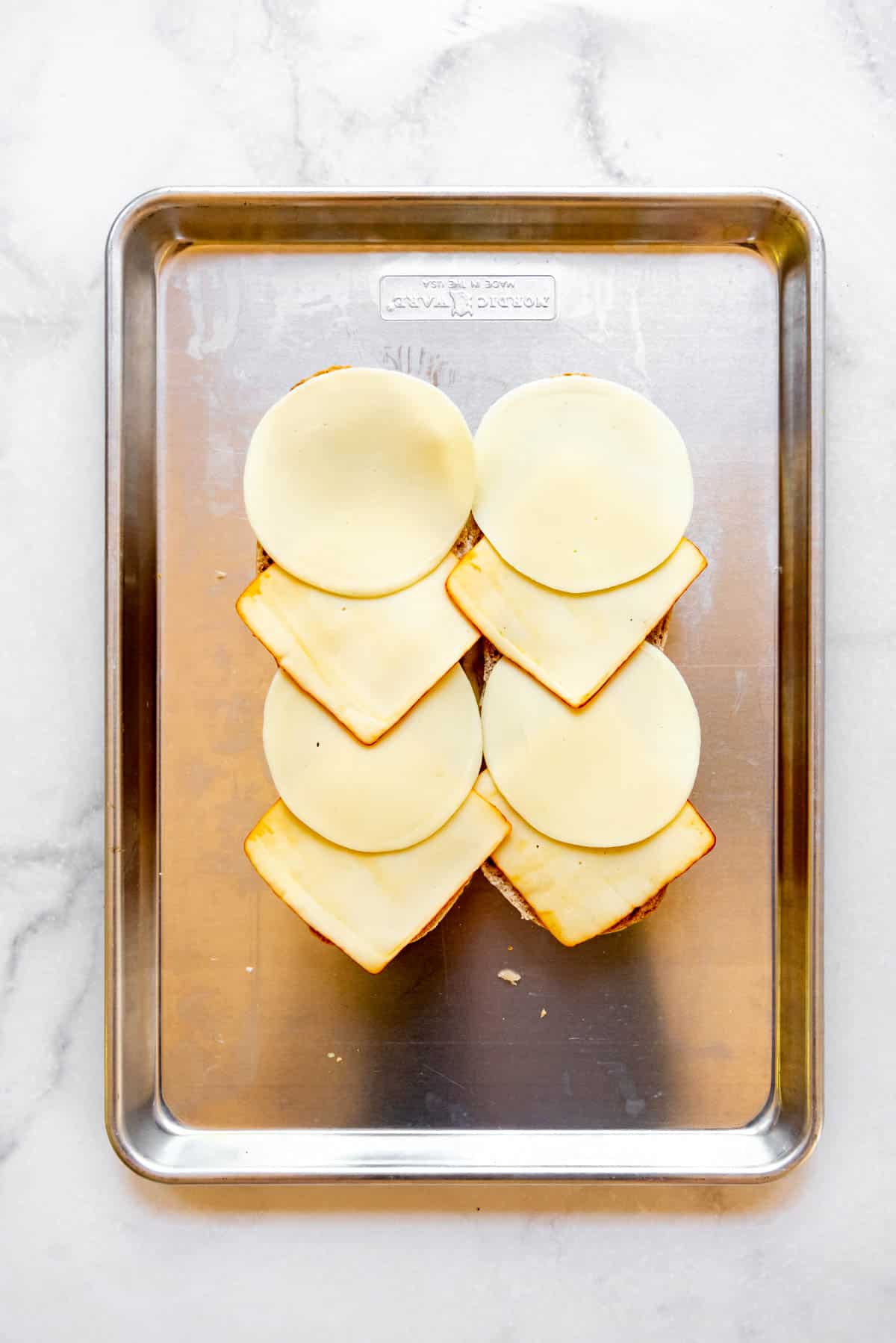 Slices of provolone and muenster cheese on a hoagie roll on a baking sheet.
