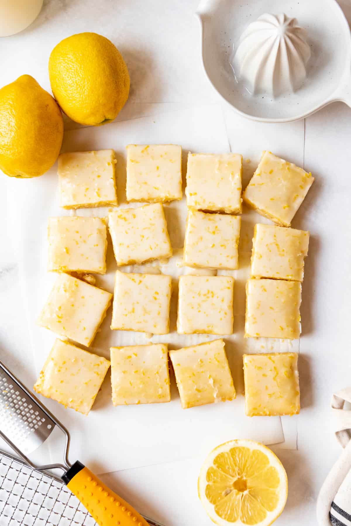 Lemon brownies cut into 16 squares surrounded by fresh lemons.