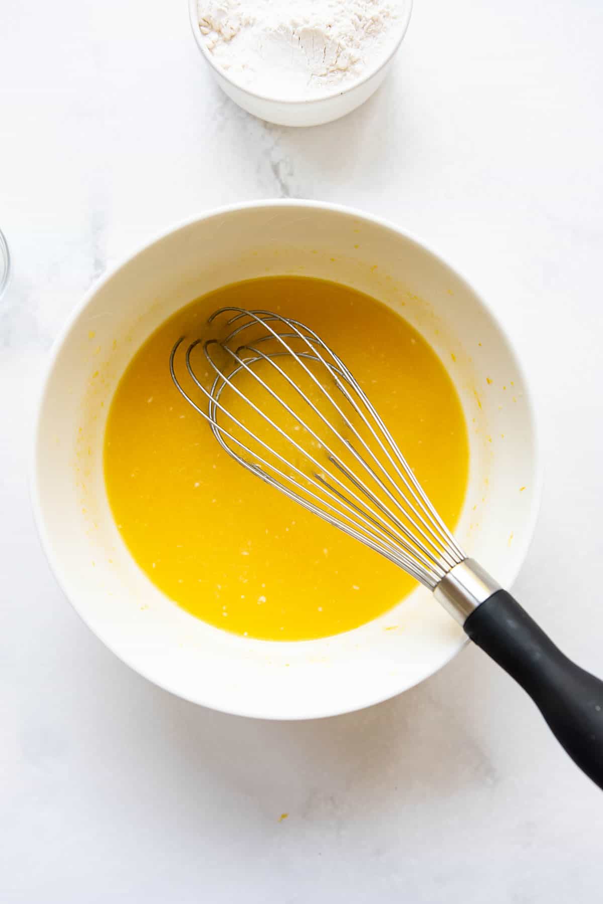 A whisk in a bowl of ingredients for lemon brownies.
