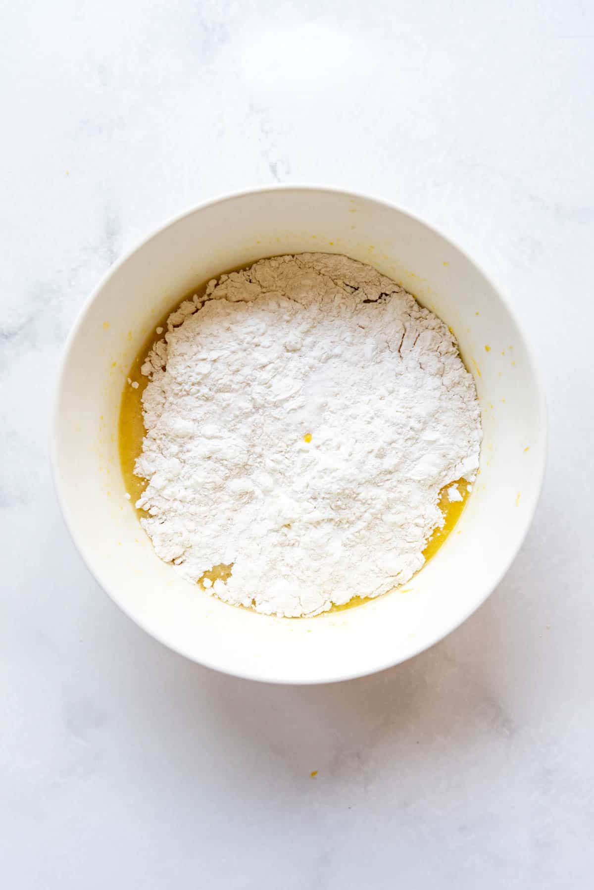 Adding dry ingredients to lemon brownie batter in a white mixing bowl.