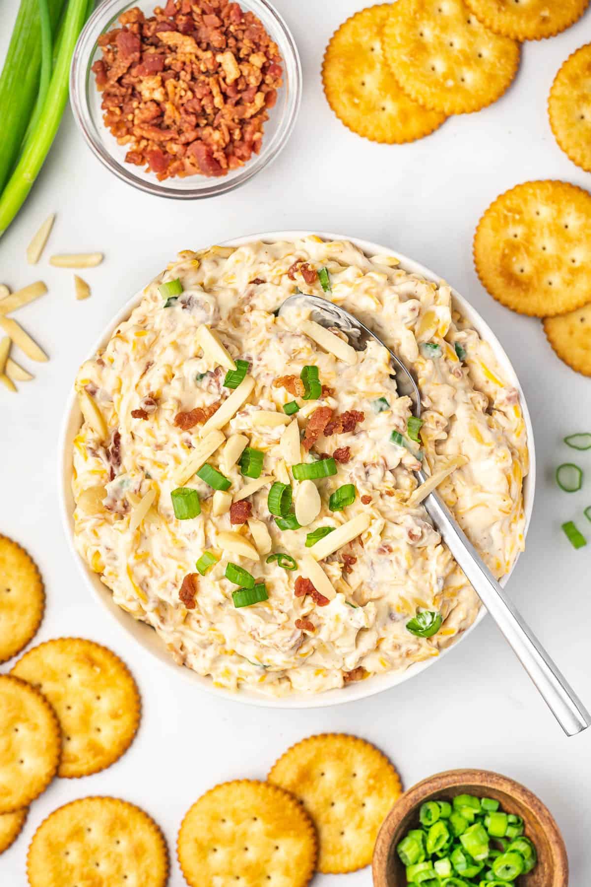 Millionaire dip in a bowl surrounded by Ritz crackers, bacon bits, and green onions.