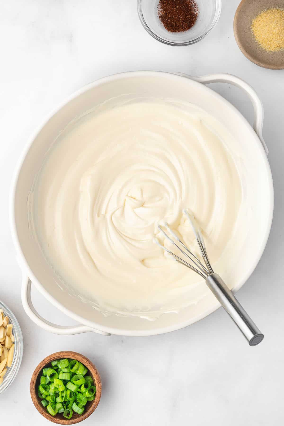Top view of a white bowl with whisked mayo and sour cream in it. 