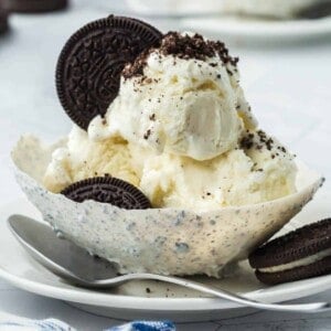 An Oreo balloon bowl filled with ice cream and crushed Oreo cookies on a plate with a spoon.