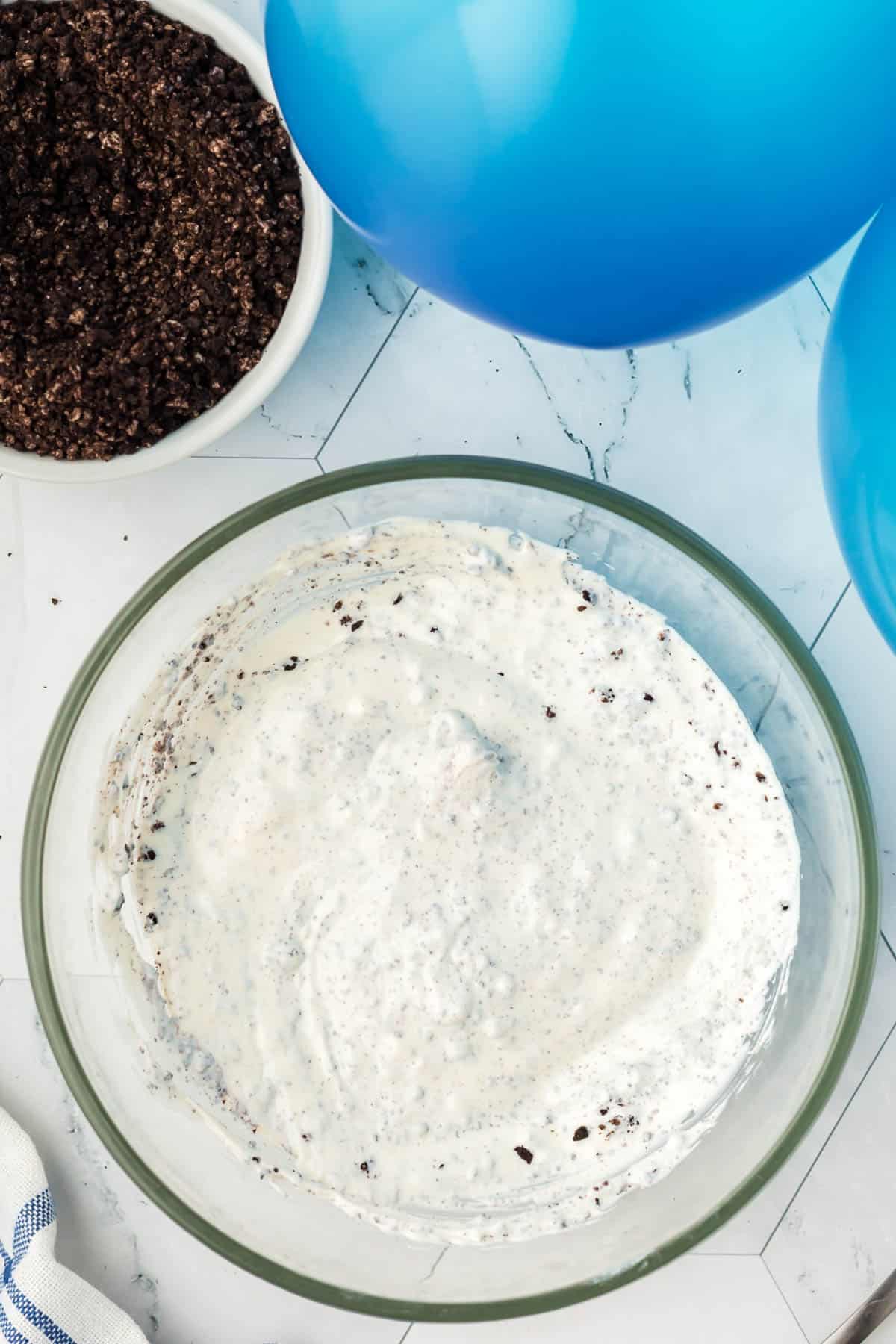 Stirring Oreo crumbs into melted white chocolate for a melted cookies and cream mixture.