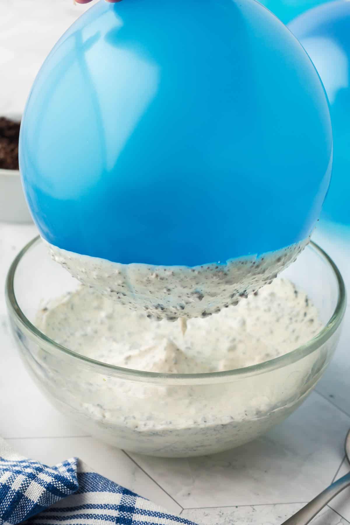 Lifting a blue balloon out of a bowl of melted cookies and cream mixture.