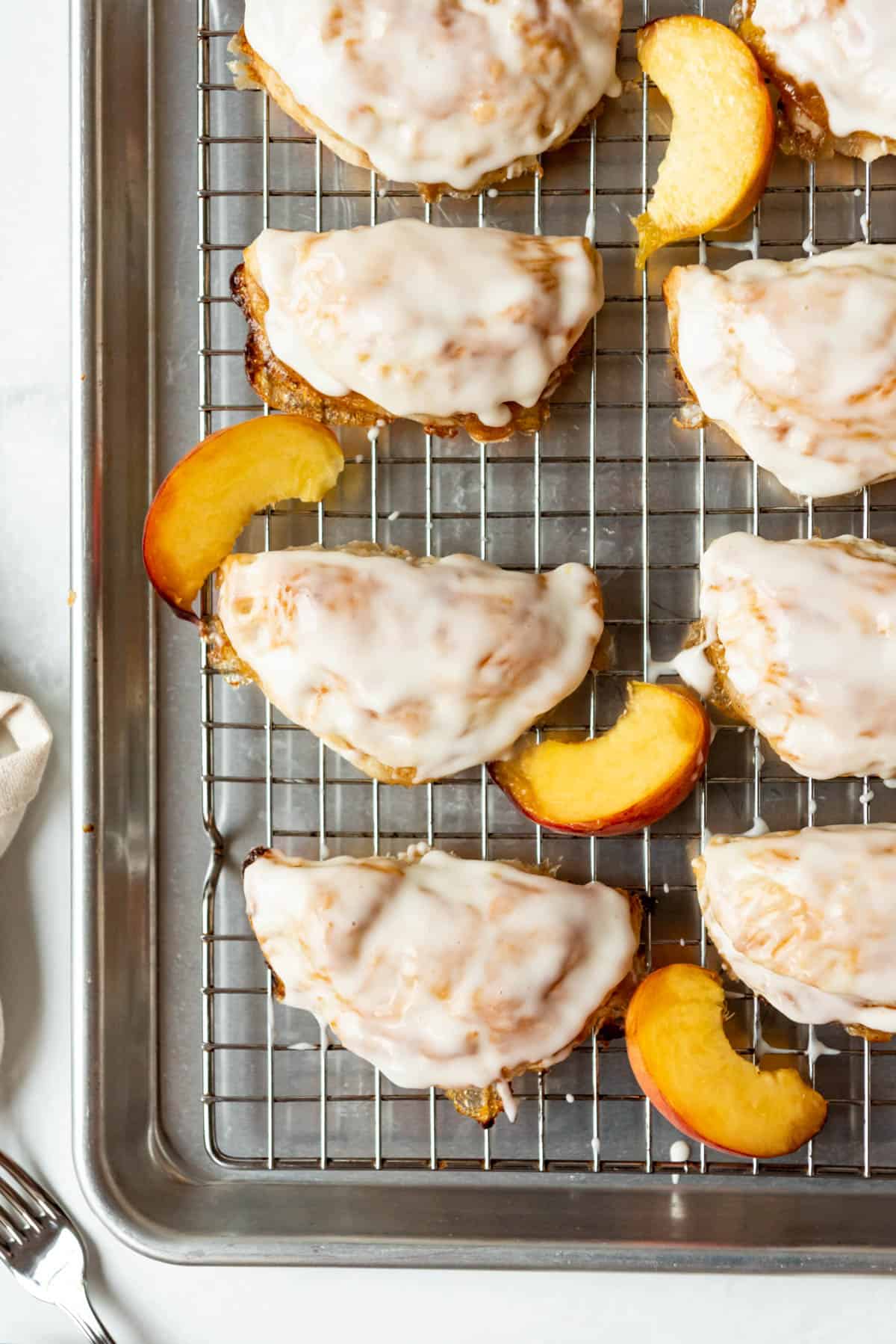A close image of glazed peach hand pies on a wire rack with slices of fresh peach.