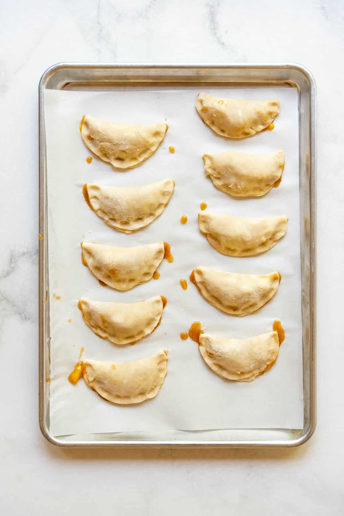 Sealed peach hand pies before baking on a baking sheet lined with parchment paper.