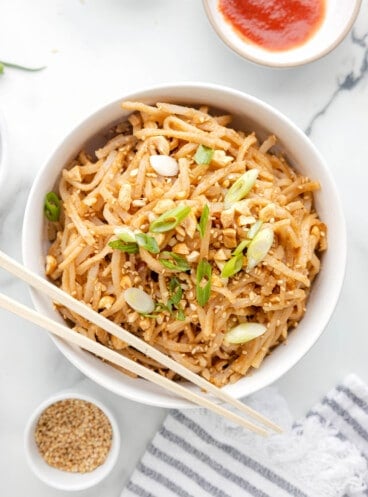 A bowl of peanut noodles with chopsticks resting on the side of the bowl.