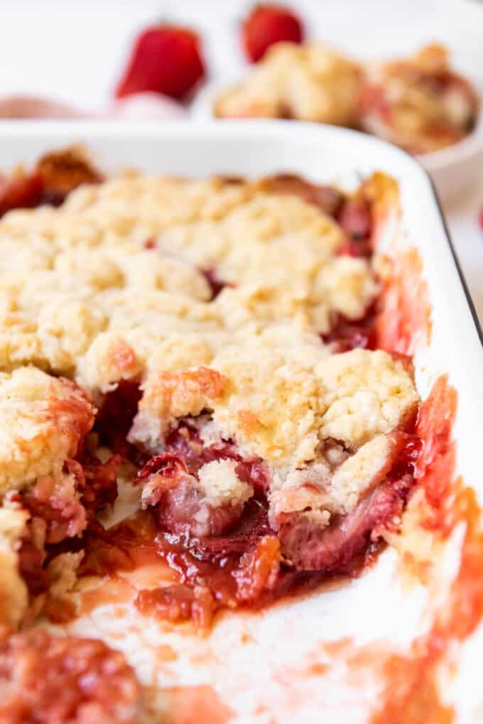 A side angle of a strawberry rhubarb cobbler with a scoop removed so you can see the fruit filling under the sweet biscuit topping.