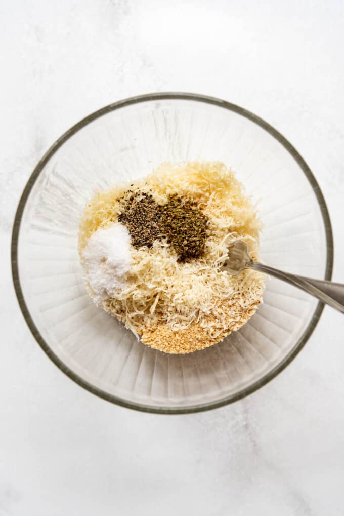 Combining breadcrumbs, parmesan cheese, and seasoning in a glass mixing bowl.