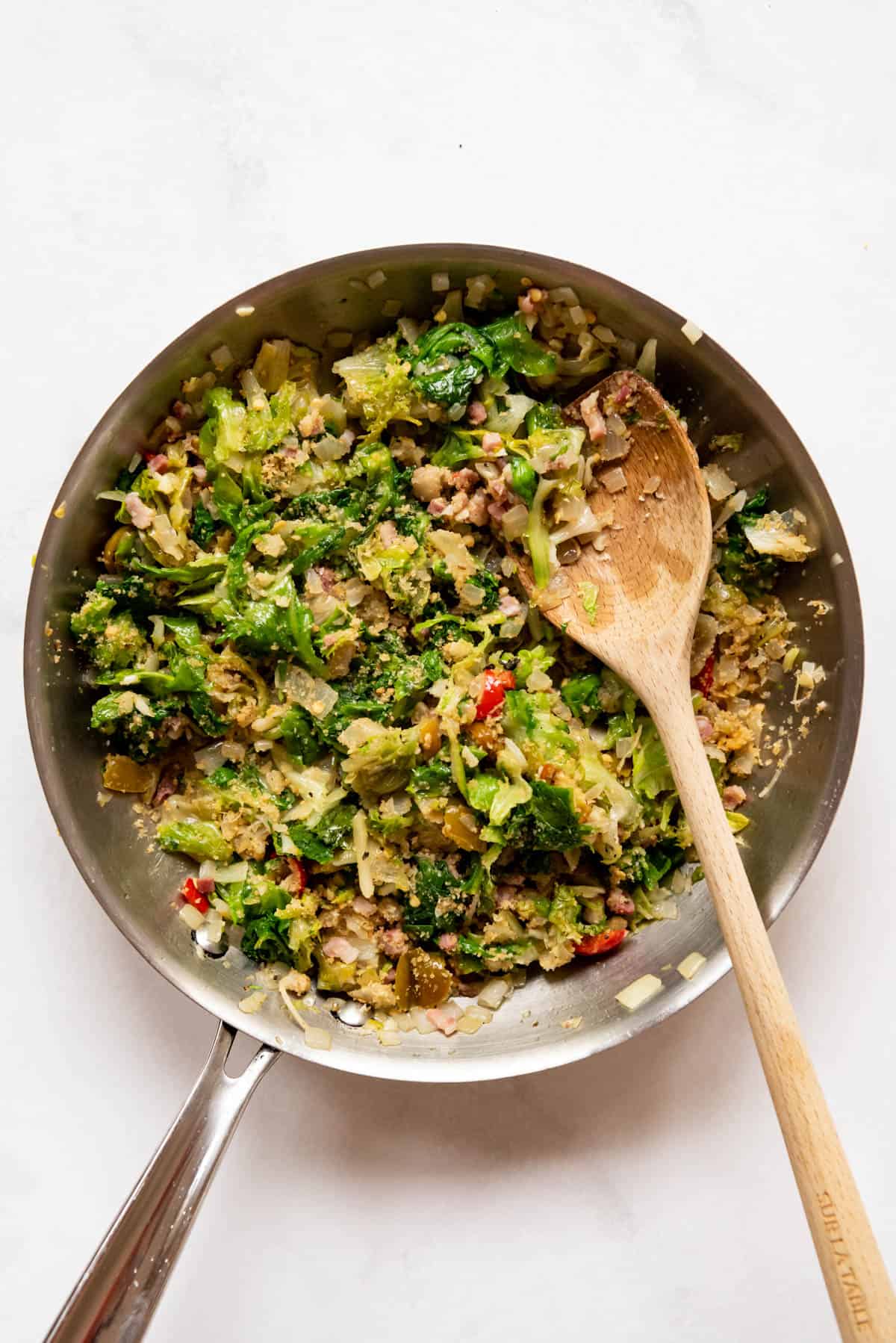 Combined Utica greens ingredients in a pan with a spoon.