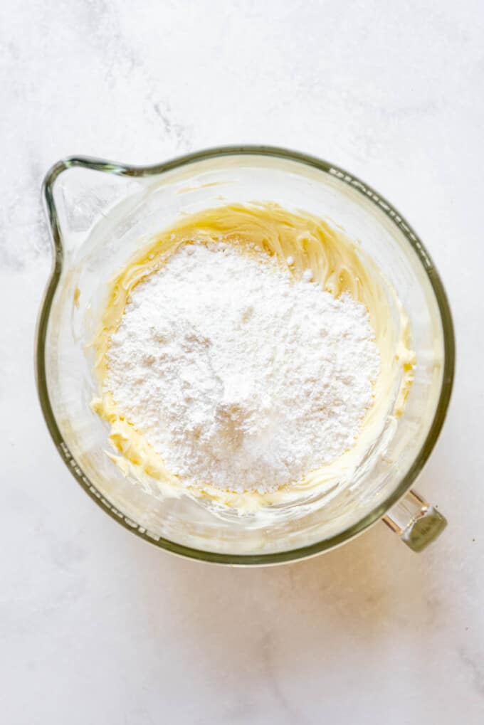 Adding powdered sugar to creamed butter and white chocolate in a mixing bowl to make frosting.